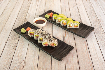 Trays of sushi uramaki california roll with poppy seeds, stuffed with Norwegian salmon, ripe avocado, cream cheese, nori seaweed and wasabi with ginseng with soy sauce