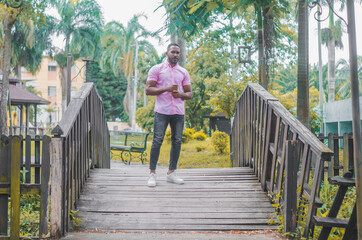attractive dark-haired man of Dominican origin walking through the bridge having a call, talking on the phone, wearing a pink shirt