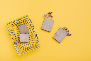 A pair of eco-friendly craft paper bags in and near a metal shopping basket with dried flowers on a yellow background. Black friday gift sales