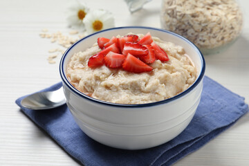 Tasty oatmeal porridge with strawberries served on white wooden table