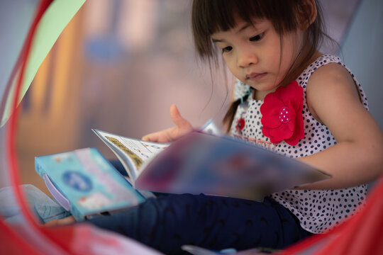 1 Asian girl, age 3 years old, enjoying a cartoon picture book.