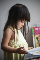 A 3-year-old Asian girl is interested in a scrapbook in her hand.