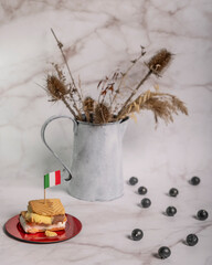 Ice cream filled cookies with over a flag of Italy and in the background a vase with dried flowers and blueberries