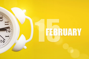 February 15th. Day 15 of month, Calendar date. White alarm clock on yellow background with calendar day. Winter month, day of the year concept.