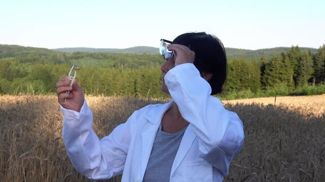 A woman scientist with glasses takes samples of wheat in an ole for study in the laboratory..