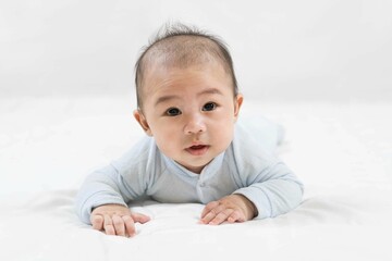 Morning Time.Adorable newborn kid during tummy time smiling happily at home.Portrait of cute smiling happy asian baby boy crawling on bed on the white blanket in bedroom.