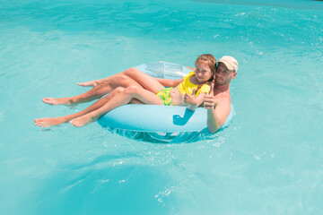 Dad and daughter swim together on a rubber ring in the pool. A man and a girl are having fun in the water of the pool.