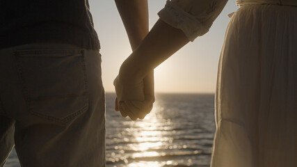 Strong man holding beloved woman by hand against sunrise over sea, happy future