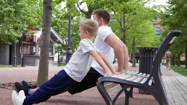 Father teaching son to do push-ups on bench outdoors