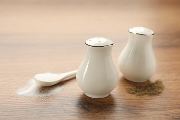 White ceramic salt and pepper shakers with spoon on wooden table, closeup