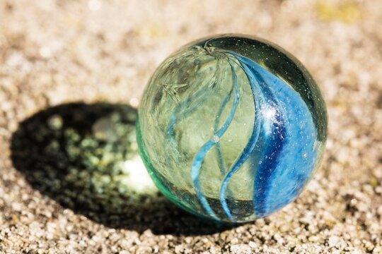 Bola de gude de vidro em piso de cimento rustico iluminada pela luz do sol.
