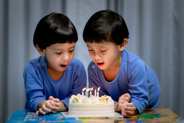 Twins adorable boy in blue shirt, celebrating his birthday, blowing candles on homemade baked cake, indoor. Birthday party for kids