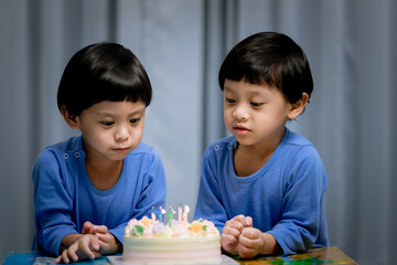 Obraz na płótnie Canvas Twins adorable boy in blue shirt, celebrating his birthday, blowing candles on homemade baked cake, indoor. Birthday party for kids