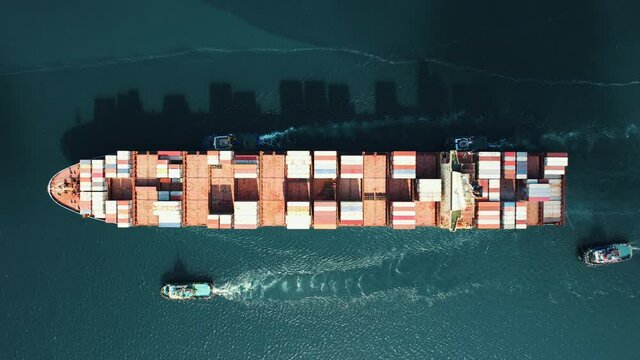 Aerial view Cargo container ship is sailing to port for unloading accompanied by pilots along canal in Black Sea. Arrival of merchant ship in city seaport with crane. Shipping by water. Top view