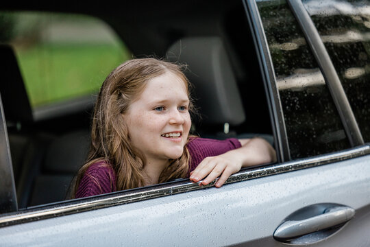 Little Caucasian Girl With Freckles And A Purple Shirt Looking Out Of A Car Window