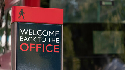 Welcome back to the office red sign in a busy commuter city center	
