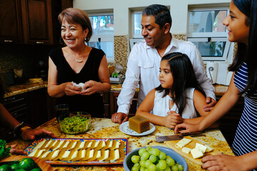 Family looking at woman while preparing appetizer in kitchen and enjoying weekend together