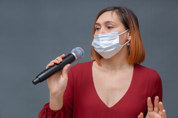 Young beautiful woman in a medical mask stands on a gray background with a phonograph in her hands