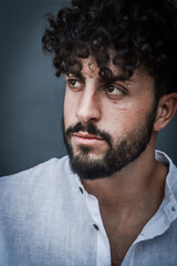 close up portrait of a serious young man with a beard and curly hair, looking to the left