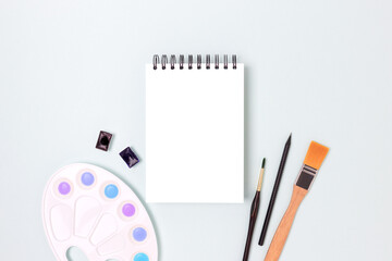 Open notepad mockup and tools for painting on a blue pastel background. Artistic workspace with copyspace.