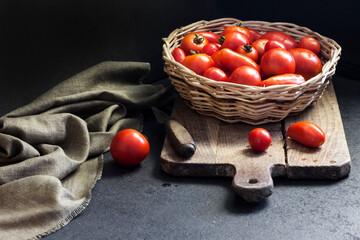 Fototapeta na wymiar Fresh red tomatoes in whicker basket on black background