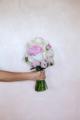 Female hand showing a bouquet with white and pink flowers as peonies and roses on white background.