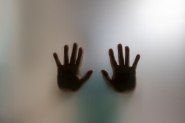 Silhouette of two blurred hands behind the frosted glass. Concept of asking for help and domestic violence.