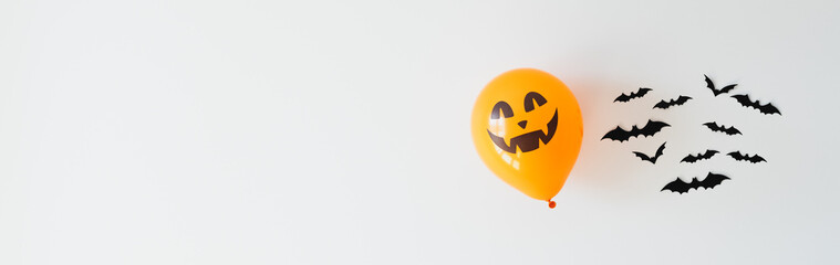 Happy Halloween holiday banner design with copy space. Bats decoration and orange balloon ghost on white wall.