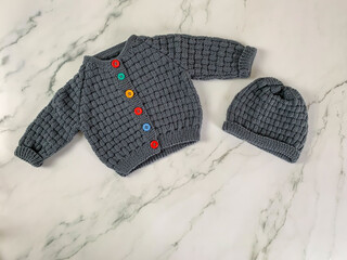 Cozy, warm grey baby sweater with colorful buttons and a cap. Knitted clothes on a table. Handmade...