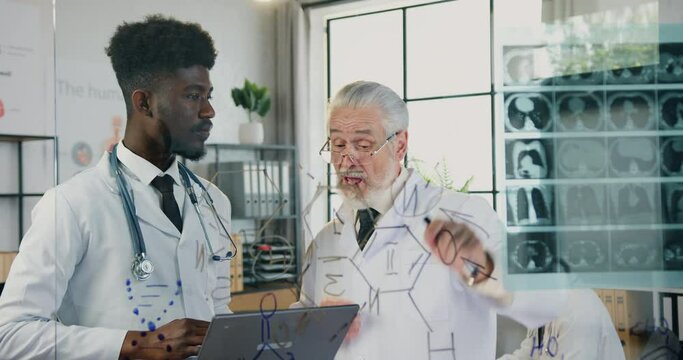 Attractive serious respected skilled bearded professor of medical university talking to his confident african american student in clinic lab and explaining x-ray scan