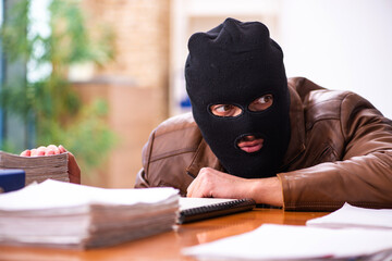 Young man in balaclava stealing information from the office