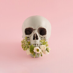 Halloween arrangement made of skull and flowers on a pink background. Halloween party concept.