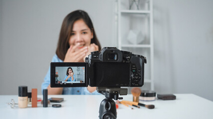 Naklejka premium Happy smiling asian woman or beauty blogger with brush and camera recording video and waving hand at home. Beauty videoblog blogging people concept.