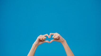 Young woman hand shows making shape of heart sending love to her lover over blue background. Copy space for place a text, message for advertisement. Advertising area, mockup promotional content.