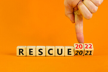 2022 rescue new year symbol. Businessman turns wooden cubes and changes words 'rescue 2021' to 'rescue 2022'. Beautiful orange background, copy space. Business, 2022 rescue new year concept.
