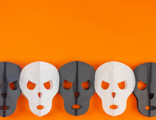 paper black and white skulls on an orange background with copy space. halloween horror and decorations concept.