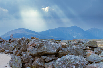 large rocks with mountains and sun rays through clouds in the background