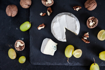 Fototapeta na wymiar Brie type of cheese. Soft cheese with grapes and walnuts on black background