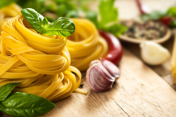 Tagliatelle and pasta on wooden table with basil leaf, pepper, garlic and parsley with copy space