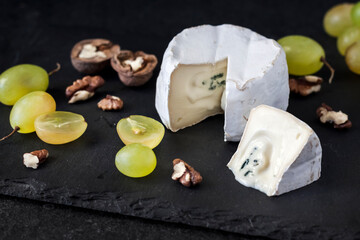 Brie type of cheese. Soft cheese with grapes and walnuts on black background