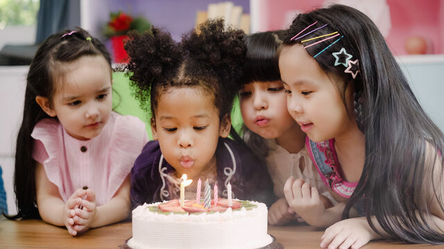 Group of children celebrate birthday's party in classroom, Multi-ethnic young boys and girls happy make a wish blow out candles on birthday cake at school. Kids celebrate birthday at school concept.