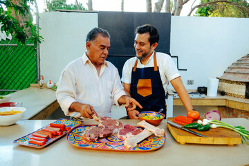 Fototapeta na wymiar Smiling mature man looking at father while preparing steaks on counter in backyard