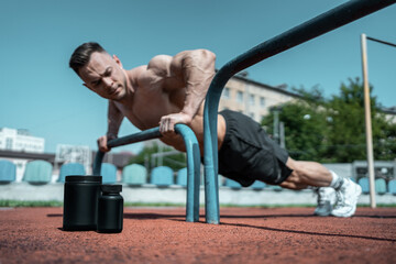 protein whey drink in black container and muscular athlete exercising outdoor