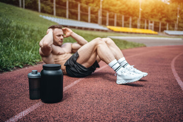 protein whey drink in black container and muscular athlete exercising outdoor