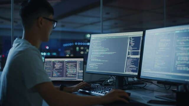Night Office: Young Japanese Man in Working on Desktop Computer. Digital Entrepreneur Typing Code, Creating Modern Software, e-Commerce App Design, e-Business Programming. Over Shoulder