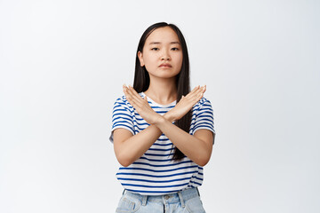 Young asian woman make cross gesture, tell to stop, prohibit action, dislike smth, standing in...
