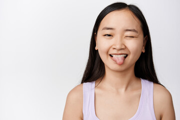 Beauty. Positive and happy asian girl winking, showing tongue and making silly faces, standing over white background, having fun