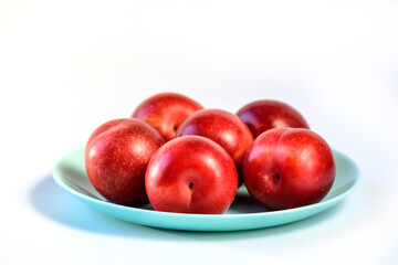 Raw Organic Red Plums on white background, fresh shiny fruits. Farm fresh organic red plums produce in plate on white background