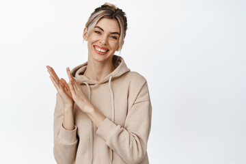 Young smiling woman applause you, looking happy and clapping hands, congratulating someone,...