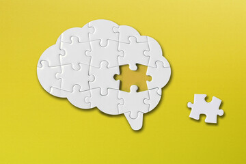 Brain shaped white jigsaw puzzle on yellow background, a missing piece of the brain puzzle, mental health and problems with memory